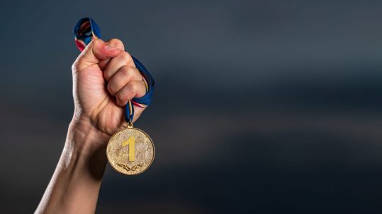 Hand holding gold medal on against cloudy twilight sky background, The winner and successful concept